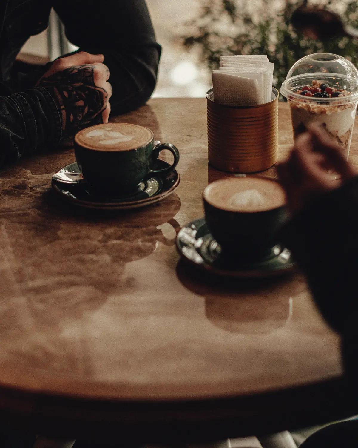 Two people at a round cafe table with cappuccinos, only their hands in view