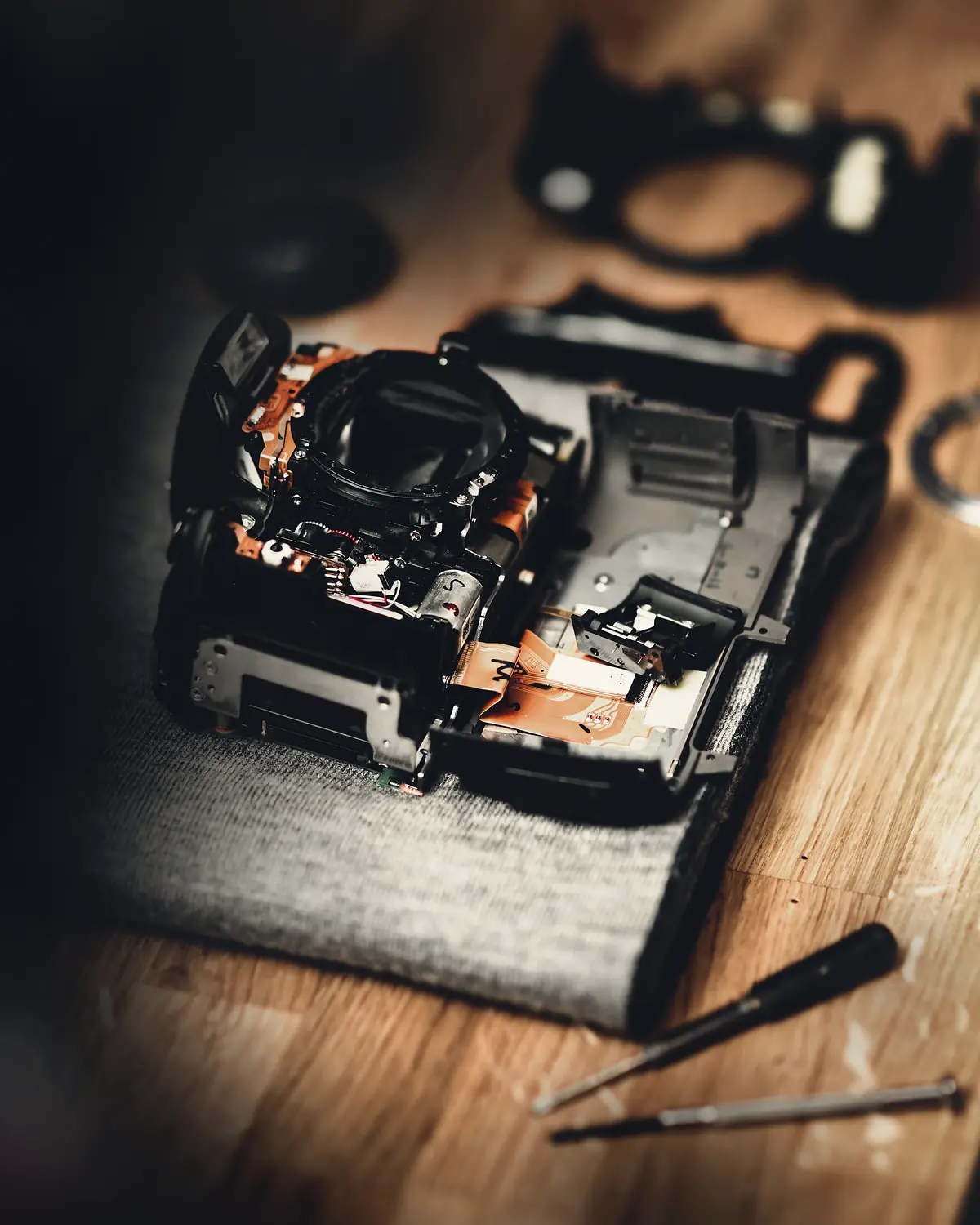 A film camera half taken apart on a wooden table, two small screwdrivers beside it
