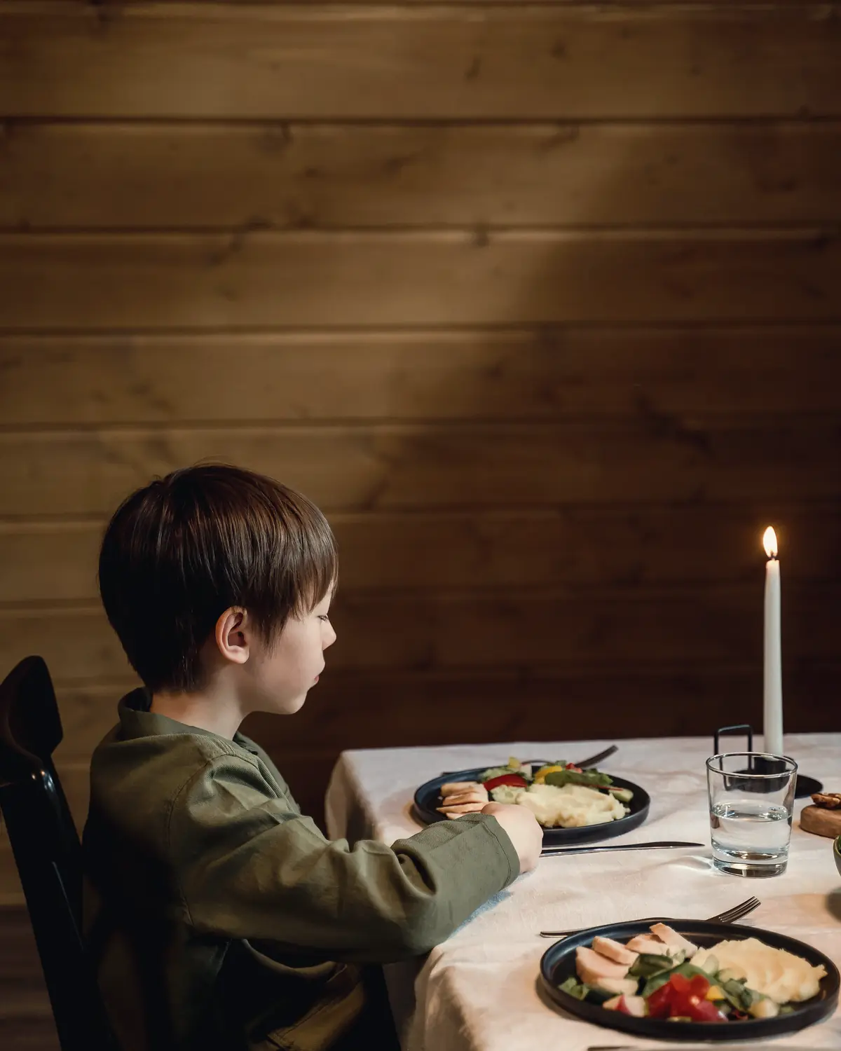A young boy eating dinner alone at a candlelit table