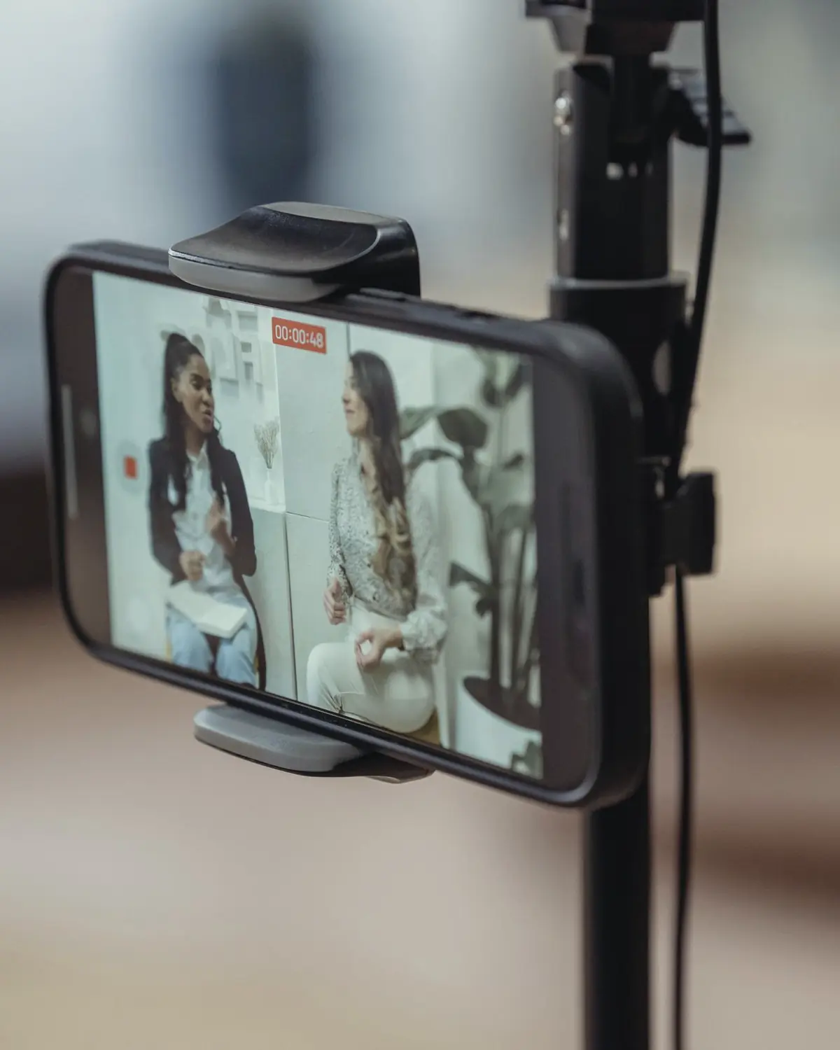 A phone on a tripod recording two people talking, the room blurred behind it