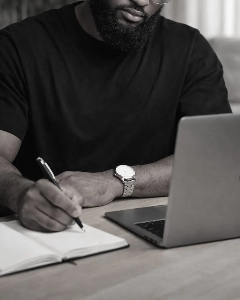 Omar writing in a notebook beside an open laptop