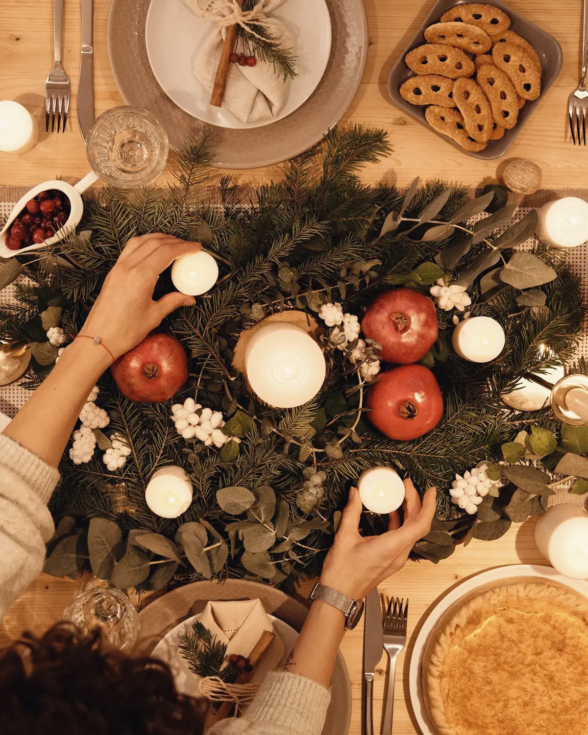 A Christmas table from above, candles being set among pine branches and pomegranates